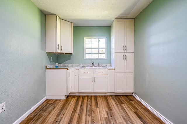 kitchen featuring white cabinetry, light stone countertops, a textured ceiling, light hardwood / wood-style floors, and sink