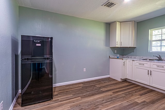 kitchen with white cabinets, black fridge, and hardwood / wood-style floors