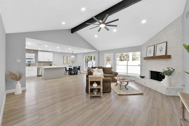 living room with beam ceiling, a brick fireplace, light wood-type flooring, and ceiling fan