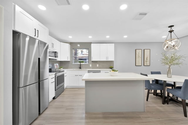 kitchen with white cabinetry, light wood-type flooring, stainless steel appliances, pendant lighting, and a center island