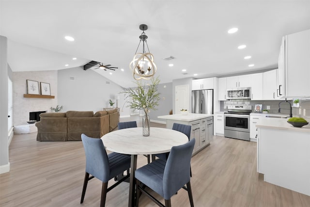 dining area with lofted ceiling, a large fireplace, ceiling fan, light wood-type flooring, and sink