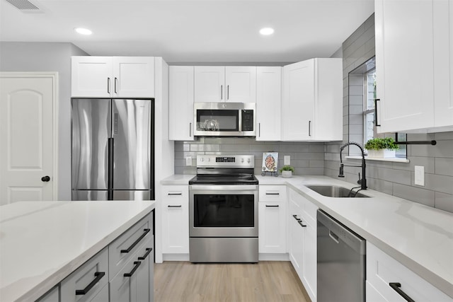 kitchen with light hardwood / wood-style floors, appliances with stainless steel finishes, sink, and white cabinets