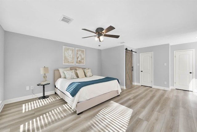 bedroom featuring ceiling fan, light hardwood / wood-style floors, and a barn door