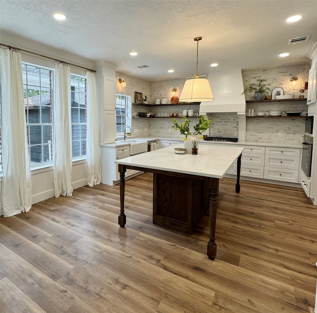 kitchen with oven, white cabinets, hanging light fixtures, a textured ceiling, and light wood-type flooring