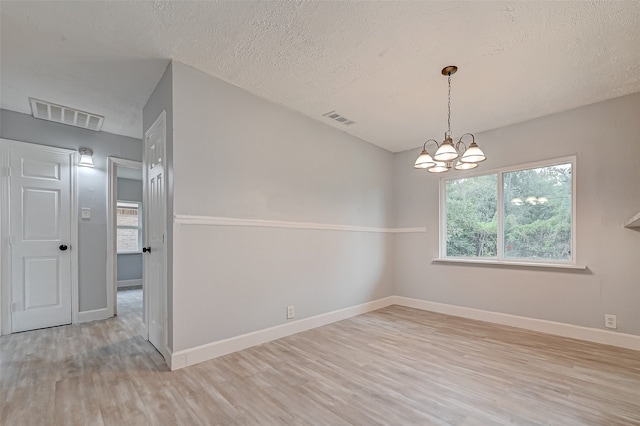 spare room featuring a textured ceiling, a chandelier, and light wood-type flooring