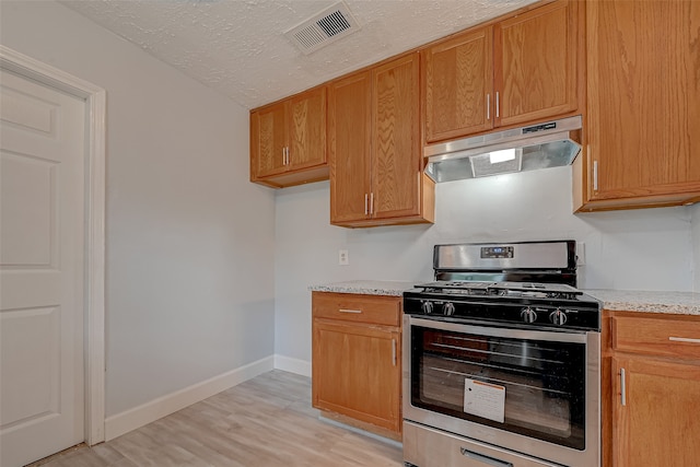 kitchen featuring gas range, light hardwood / wood-style flooring, a textured ceiling, and light stone countertops