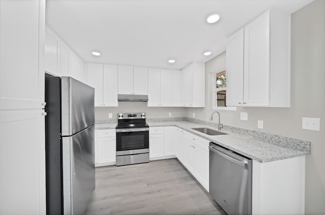 kitchen with sink, white cabinets, light wood-type flooring, appliances with stainless steel finishes, and light stone counters