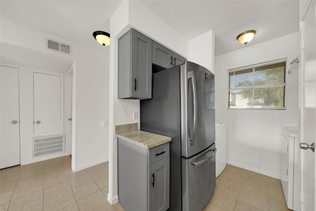 kitchen with gray cabinets, light tile patterned flooring, stainless steel fridge, and light stone counters