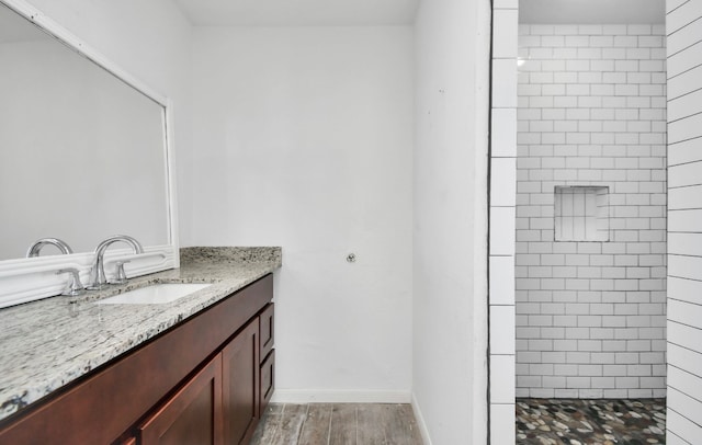 bathroom featuring vanity, a tile shower, and wood-type flooring