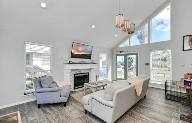 living room with high vaulted ceiling, hardwood / wood-style flooring, a wealth of natural light, and a tile fireplace