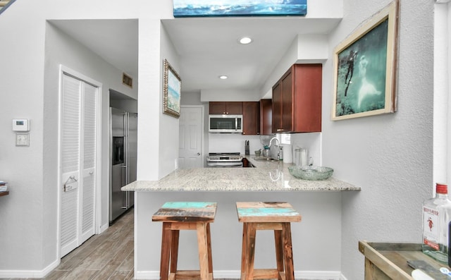 kitchen with sink, kitchen peninsula, a breakfast bar area, stainless steel appliances, and light hardwood / wood-style flooring