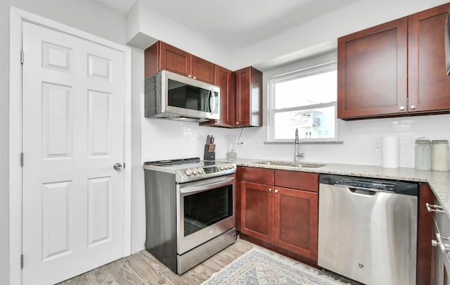 kitchen with stainless steel appliances, backsplash, sink, light stone countertops, and light hardwood / wood-style floors