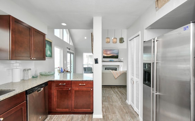 kitchen featuring light stone countertops, kitchen peninsula, light hardwood / wood-style floors, stainless steel appliances, and vaulted ceiling