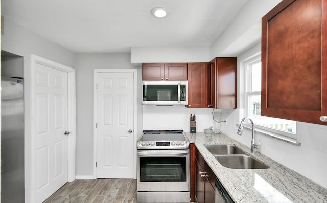 kitchen with decorative backsplash, light stone counters, appliances with stainless steel finishes, light hardwood / wood-style floors, and sink