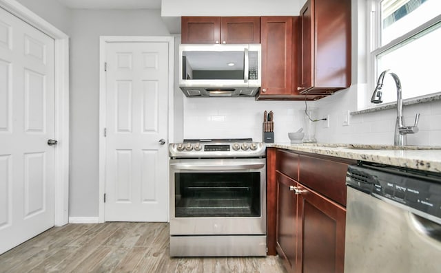 kitchen featuring backsplash, light stone counters, stainless steel appliances, and light hardwood / wood-style floors