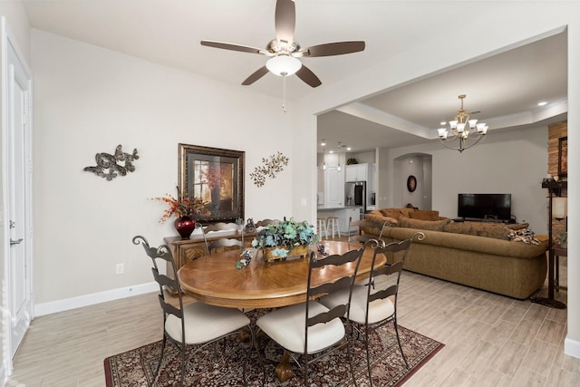 dining area featuring ceiling fan with notable chandelier, a raised ceiling, and light hardwood / wood-style flooring