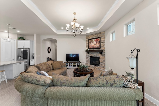 living room with a raised ceiling, a stone fireplace, ornamental molding, a notable chandelier, and light hardwood / wood-style floors