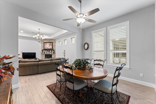 dining area featuring a fireplace, ceiling fan with notable chandelier, and light hardwood / wood-style floors