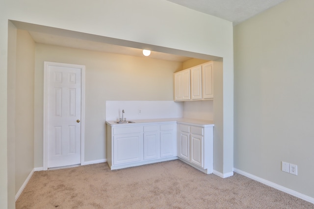 kitchen with sink, light colored carpet, and white cabinets