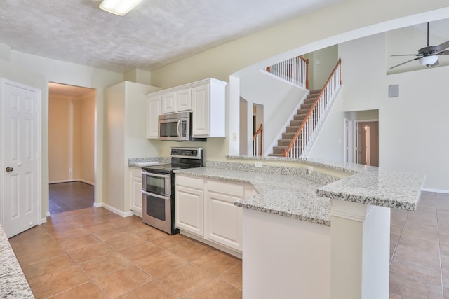 kitchen featuring light stone countertops, appliances with stainless steel finishes, kitchen peninsula, and white cabinetry