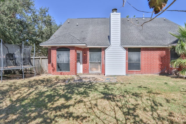 rear view of property with a yard and a trampoline