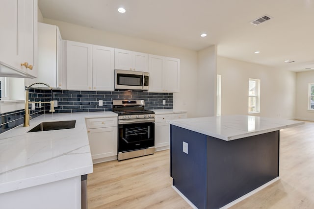 kitchen with white cabinets, light stone countertops, light hardwood / wood-style flooring, stainless steel appliances, and a center island