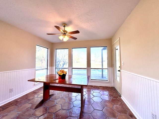 unfurnished dining area with ceiling fan and a textured ceiling