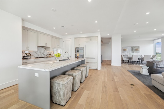 kitchen featuring a large island with sink, a kitchen bar, appliances with stainless steel finishes, light hardwood / wood-style floors, and tasteful backsplash