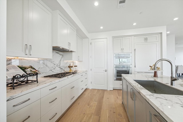 kitchen featuring visible vents, under cabinet range hood, a sink, light wood finished floors, and appliances with stainless steel finishes