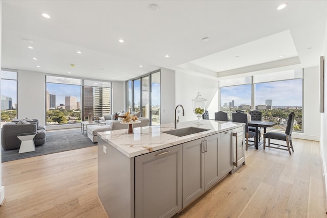 kitchen with a kitchen island with sink, sink, light stone countertops, gray cabinets, and light hardwood / wood-style floors