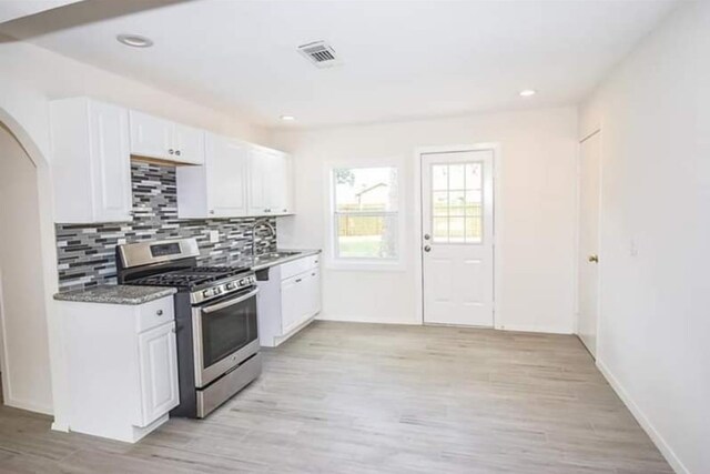 kitchen with stainless steel range with gas stovetop, light hardwood / wood-style floors, white cabinetry, and dark stone counters