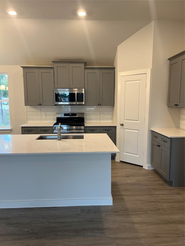 kitchen with gray cabinetry, appliances with stainless steel finishes, lofted ceiling, dark wood-type flooring, and decorative backsplash