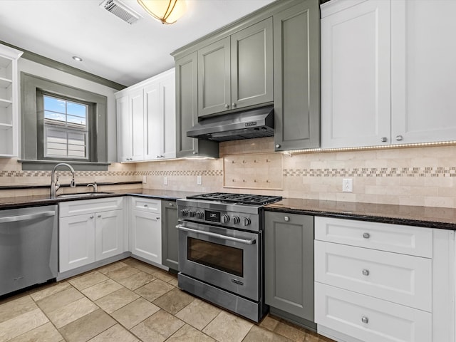 kitchen with stainless steel appliances, dark stone counters, white cabinets, sink, and tasteful backsplash