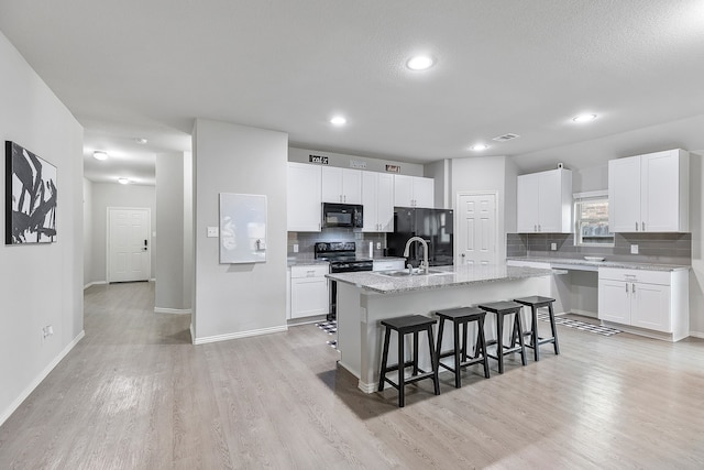 kitchen with white cabinetry, black appliances, a center island with sink, and a kitchen breakfast bar