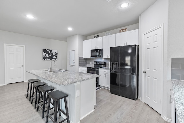 kitchen with white cabinetry, black appliances, sink, and a center island with sink