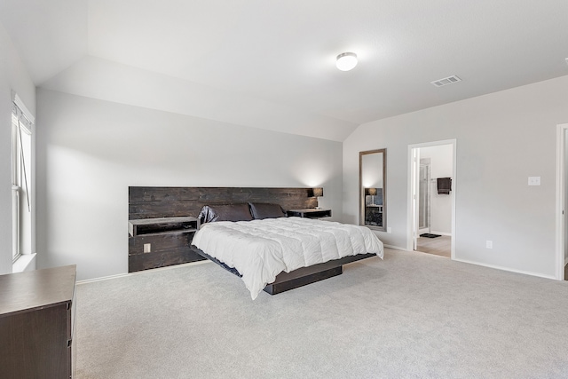 bedroom with lofted ceiling, light carpet, and connected bathroom