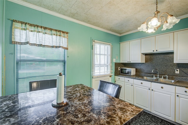 kitchen featuring a notable chandelier, white cabinetry, sink, crown molding, and decorative light fixtures