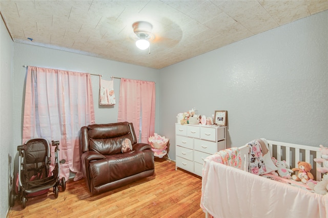 bedroom featuring light hardwood / wood-style flooring, a nursery area, and ceiling fan