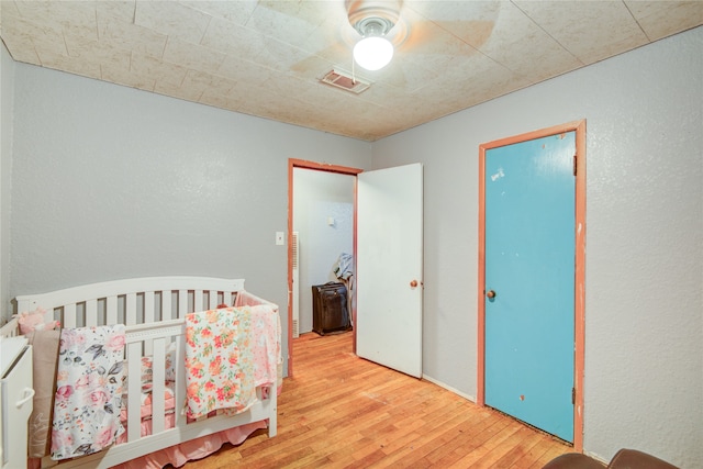 bedroom with hardwood / wood-style floors, a nursery area, and ceiling fan