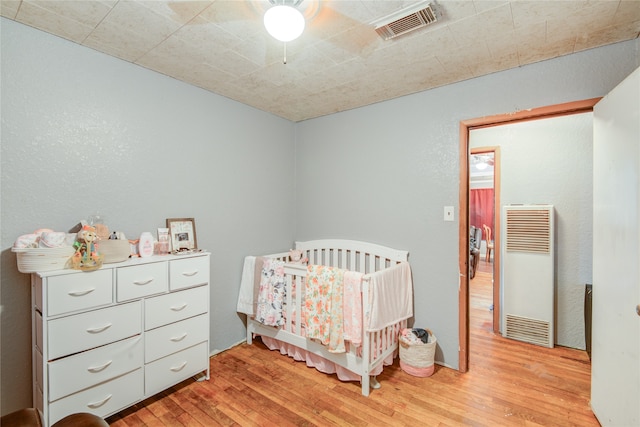 bedroom with ceiling fan, light hardwood / wood-style floors, and a crib