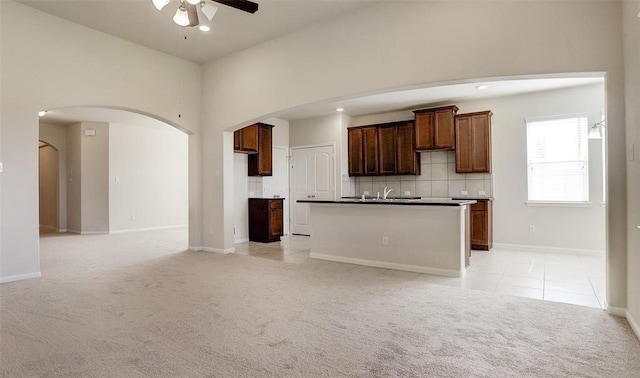 kitchen featuring decorative backsplash, a kitchen island with sink, sink, light colored carpet, and ceiling fan