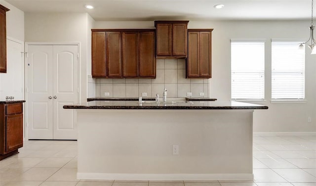 kitchen with decorative backsplash, dark stone counters, a center island with sink, and hanging light fixtures