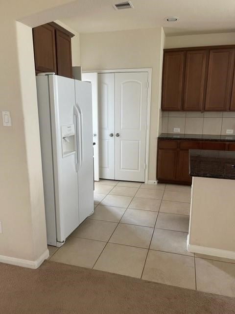 kitchen with white refrigerator with ice dispenser, light tile patterned floors, and tasteful backsplash