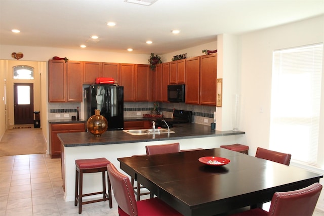 kitchen featuring sink, kitchen peninsula, black appliances, and a kitchen bar