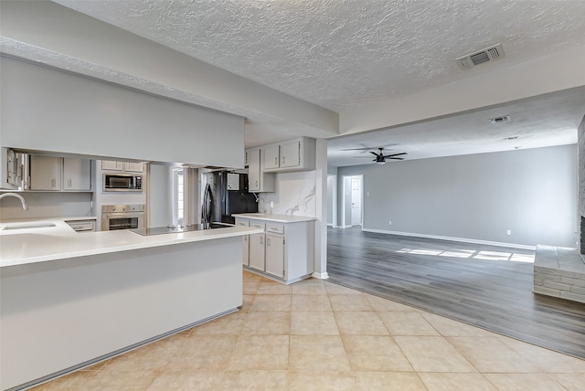 kitchen with black appliances, light wood-type flooring, a textured ceiling, kitchen peninsula, and ceiling fan