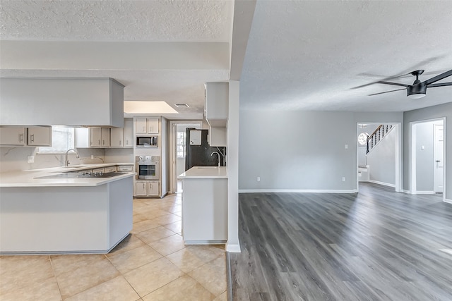 kitchen with kitchen peninsula, stainless steel appliances, a textured ceiling, light hardwood / wood-style floors, and ceiling fan