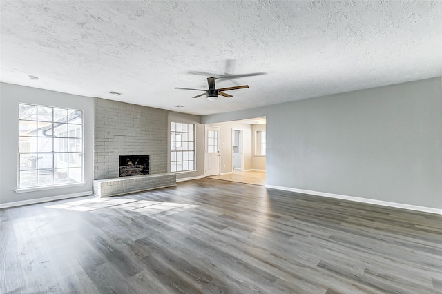 unfurnished living room featuring ceiling fan, a textured ceiling, dark hardwood / wood-style flooring, and a brick fireplace