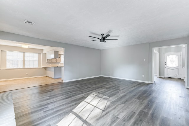 unfurnished living room featuring dark wood-type flooring, ceiling fan, and a textured ceiling