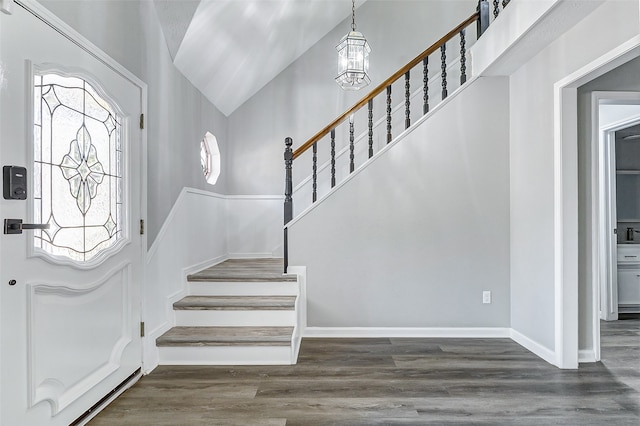 foyer entrance with a notable chandelier, high vaulted ceiling, and dark wood-type flooring