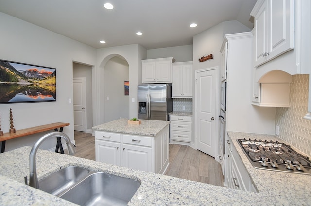 kitchen with appliances with stainless steel finishes, sink, white cabinetry, decorative backsplash, and light hardwood / wood-style flooring